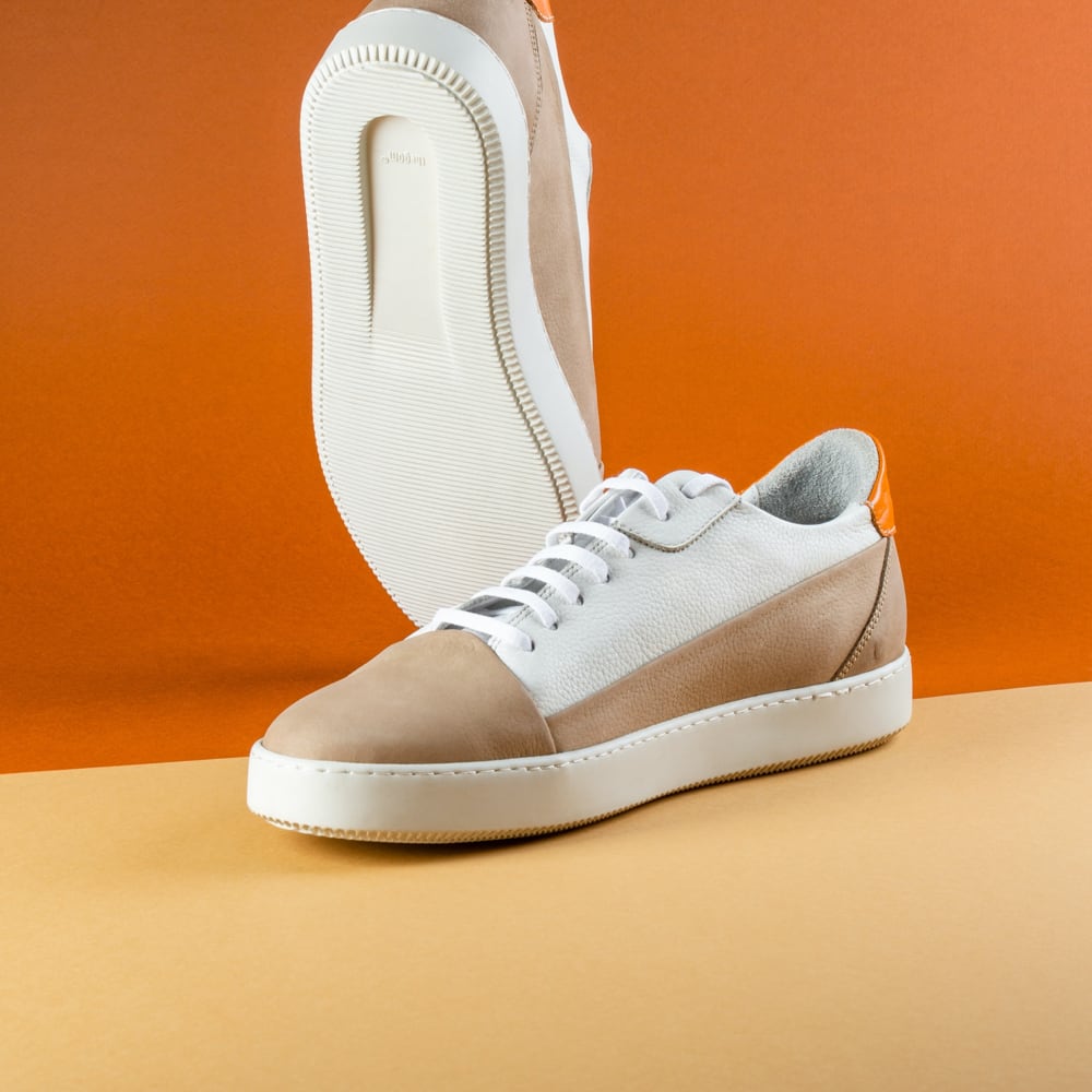 White and beige sneakers with an orange accent, displayed against an orange background.