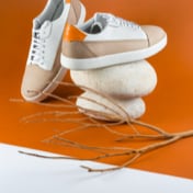 Thumbnail of white sneakers stacked on smooth stones, with an orange backdrop.